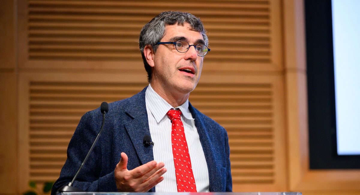 A person in a suit and red tie speaks at a podium