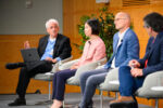 An academic panel sits in discussion on stage