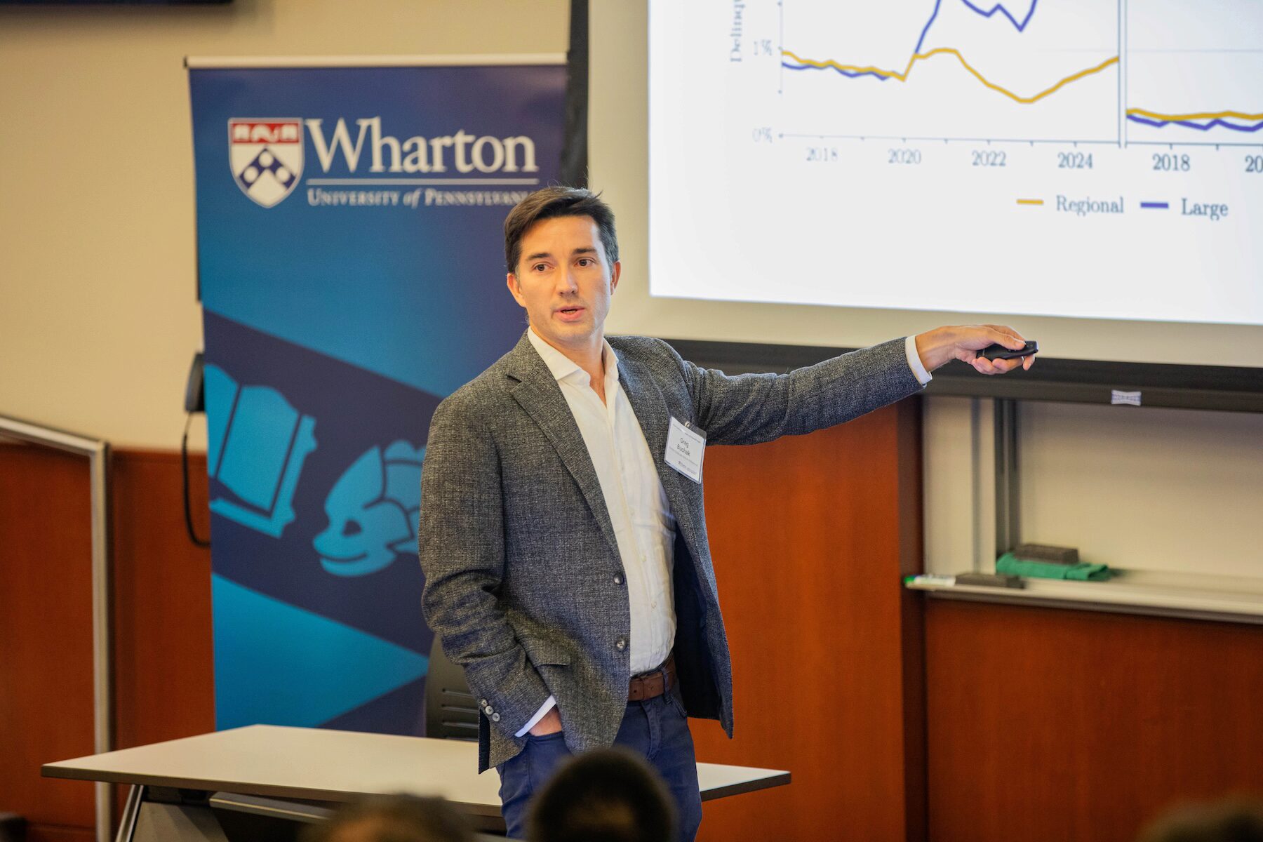 A speaker points a remote clicker toward a presentation while looking outward